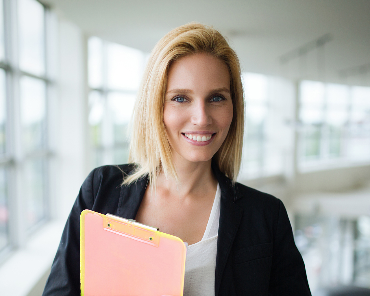 Successful smiling business woman at work holding documents, standing near window in office